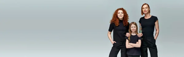 Three generations of stylish women in matching clothes standing on grey background, banner — Stock Photo
