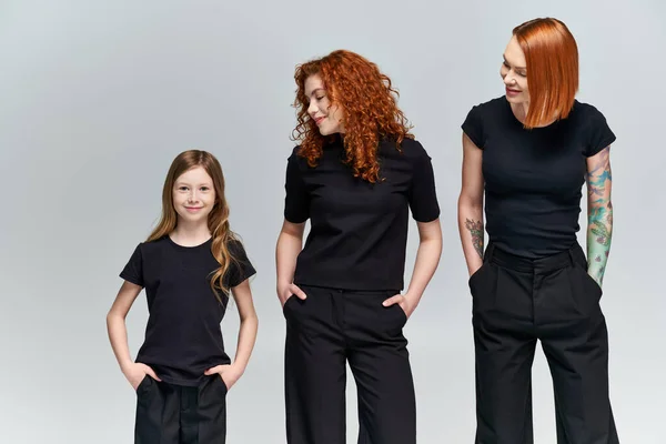 Três gerações, mulheres e menina posando com as mãos nos bolsos em correspondência traje no fundo cinza — Fotografia de Stock