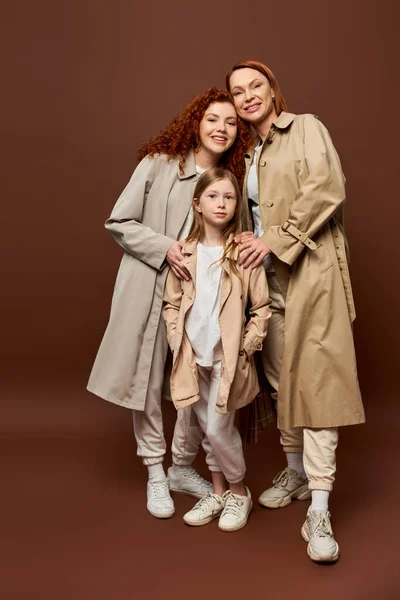 Three generations, happy redhead family posing in autumn trench coats on grey background, fashion — Stock Photo
