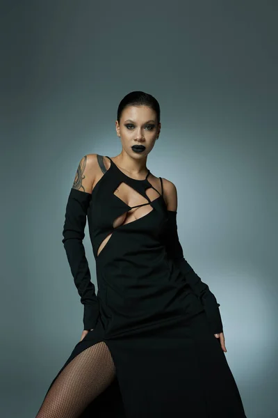 Mulher sensual em vestido preto e maquiagem misteriosa escuro olhando para a câmera em cinza, conceito halloween — Fotografia de Stock