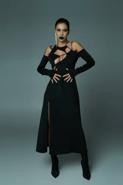 In voller Länge betörende Frau in schwarzem Zaubererkleid und Make-up auf grau, Halloween-Konzept — Stockfoto