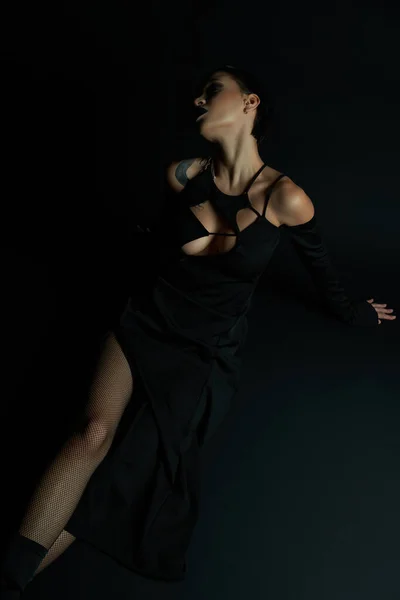 Leidenschaftliche tätowierte Frau in sexy Halloween-Kleid sitzt auf schwarzem Hintergrund, gotische Schönheit — Stockfoto