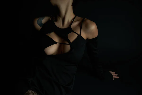 Vue recadrée de femme tatouée sexy en robe de Halloween élégant assis sur fond noir en studio — Photo de stock