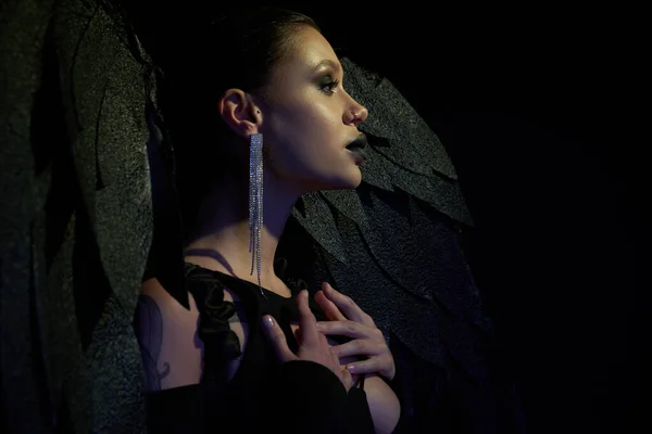 Profilo di donna sexy in orecchino lucido e costume di Halloween di angelo caduto con le ali su nero — Foto stock
