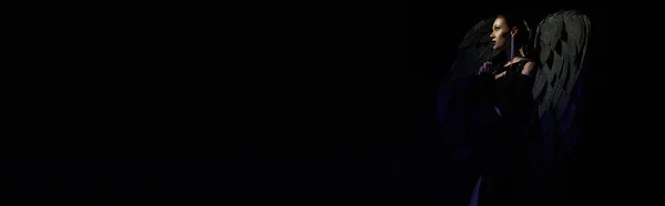 Vue latérale de la femme en costume d'ange déchu priant sur fond noir, beauté démoniaque, bannière — Photo de stock