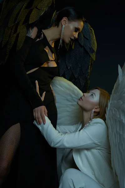 Women in Halloween costumes, dark demon tempting holy angel on black backdrop, good vs evil concept — Stock Photo