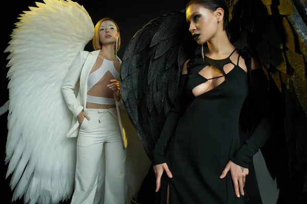 Mujeres disfrazadas de ángel y demonio sobre fondo negro, batalla bíblica del concepto del bien vs el mal - foto de stock