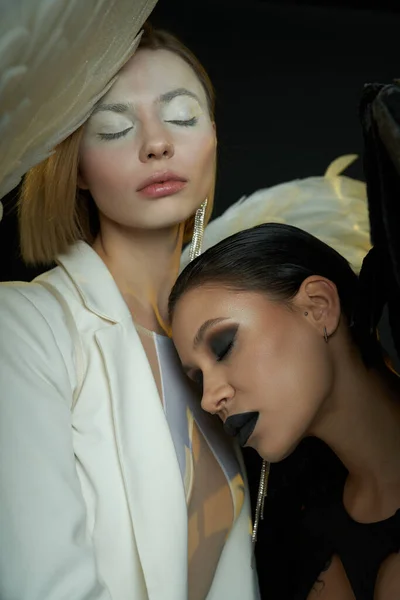 Ангельская красота и демоническое обаяние, женщины в костюмах крылатых существ с закрытыми глазами на черном — стоковое фото
