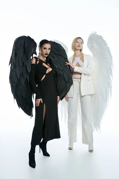 Mujeres en disfraces de Halloween de criaturas bíblicas aladas en blanco, la belleza angelical y el encanto demoníaco - foto de stock