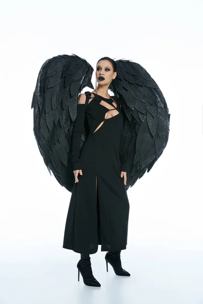 In voller Länge geheimnisvolle Frau im Kostüm eines schwarzen geflügelten Dämons, der vor weißem Hintergrund wegschaut — Stockfoto