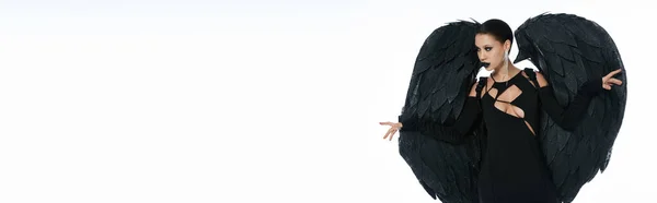 Belleza demoníaca, mujer disfrazada de criatura alada negra posando sobre fondo blanco, pancarta - foto de stock