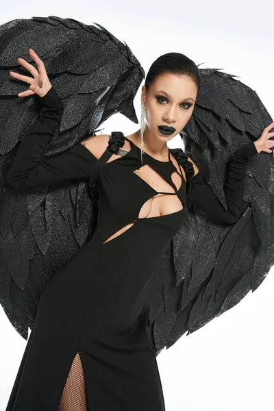 Темная красавица, женщина в костюме падшего ангела с черными крыльями, смотрящая в камеру на белом — стоковое фото