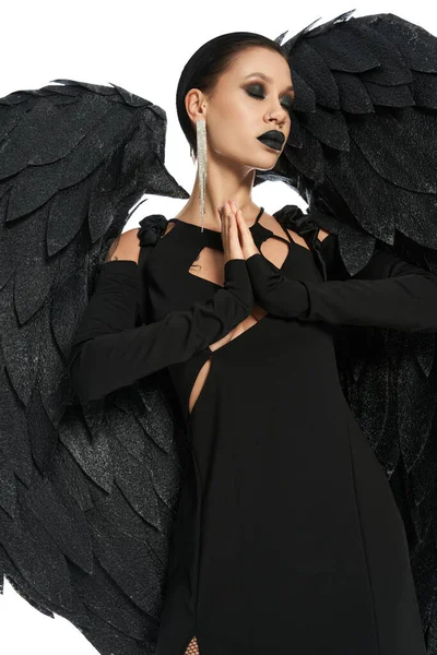 Mujer disfrazada de ángel caído con alas negras rezando con los ojos cerrados en blanco, bandera - foto de stock