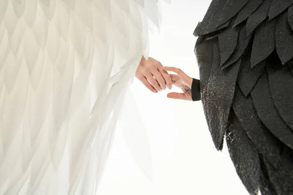 Обрізаний вид на ангела та демона з чорними та світлими крилами, що тримають руки на білому — стокове фото