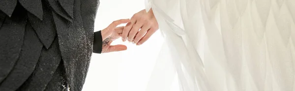 Cropped view of angel and demon with black and light wings holding hands on white, banner — Stock Photo