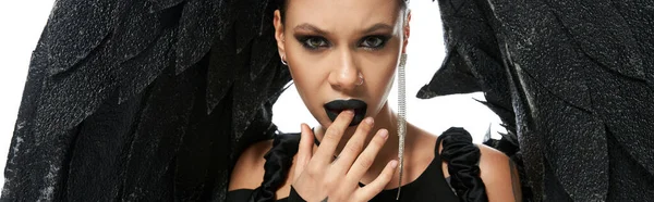 Portrait of seductive woman in dark makeup and costume of black demon touching lips on white, banner — Stock Photo