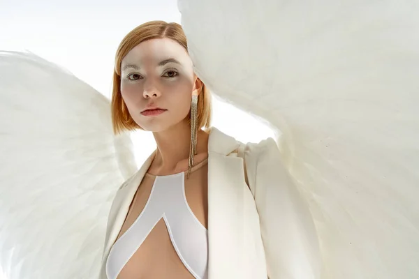 Woman in costume of light winged angel looking at camera on white, magic charm and purity — Stock Photo