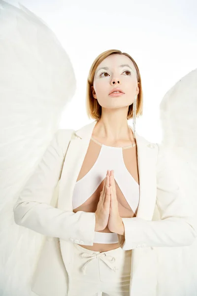 Жінка з ангельським обличчям і світлими крилами дивиться і молиться на білому тлі — стокове фото