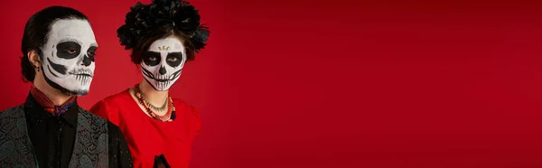 Dia de los muertos couple, woman in eerie skull makeup and black wreath near man on red, banner — Stock Photo