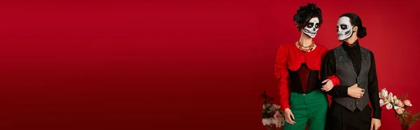 Casal elegante na maquiagem catrina posando perto de flores no vermelho, dia de los muertos festival, banner — Fotografia de Stock