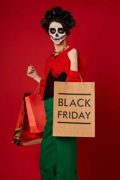 Mulher elegante em dia de los muertos maquiagem de pé com sacos de compras em vermelho, venda sexta-feira preta — Fotografia de Stock