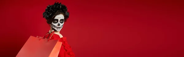 Portrait de femme dans un maquillage effrayant du crâne et une couronne noire avec des sacs à provisions sur rouge, bannière — Photo de stock