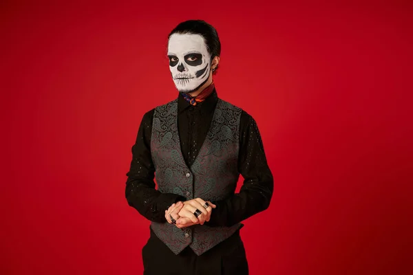 Homem elegante em misteriosa maquiagem crânio dia de los muertos olhando para a câmera em vermelho, tradição mexicana — Fotografia de Stock