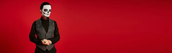 Елегантний чоловік у солоному діапазоні де лос мюарт цукровий череп макіяж дивиться на камеру на червоному, банер — стокове фото