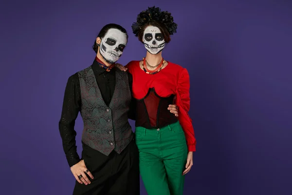 Dia de los muertos couple, man in sugar skull makeup embracing woman in black wreath on blue — Stock Photo