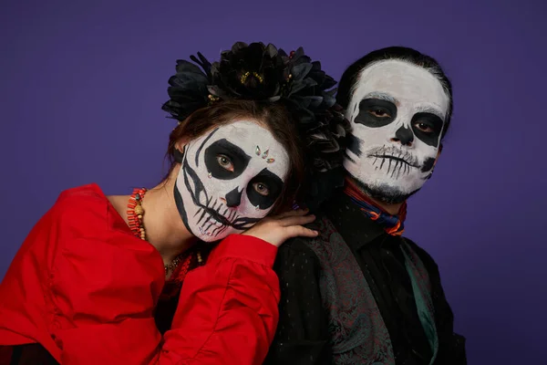 Woman in sugar skull makeup and black wreath leaning on shoulder of eerie man on blue, Day of Dead — Stock Photo