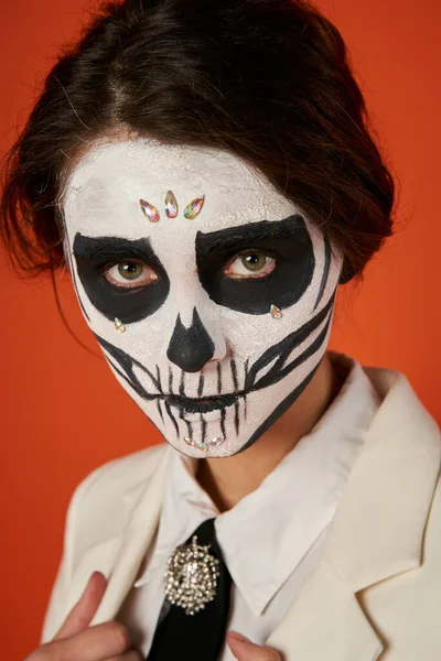 Portrait of woman in scary sugar skull makeup looking at camera on red, dia de los muertos tradition — Stock Photo