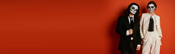 Couple à la mode dans dia de los muertos crâne de sucre maquillage et costumes regardant caméra sur rouge, bannière — Photo de stock
