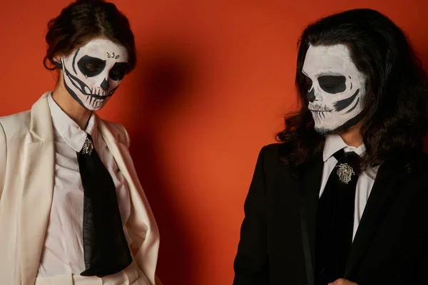 Spooky couple in catrina makeup and elegant suits with ties on red, dia de los muertos tradition — Stock Photo
