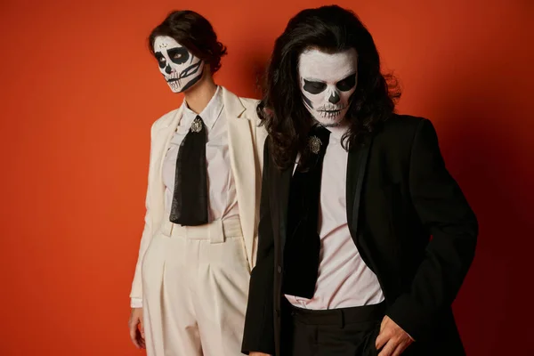 Couple in scary sugar skull makeup and black and white suits on red, dia de lost muertos fest — Stock Photo