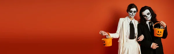 Casal elegante na maquiagem dia de los muertos e ternos de pé com baldes de doces no vermelho, banner — Fotografia de Stock