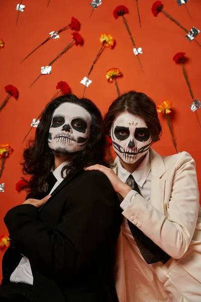 Casal assustador na maquiagem dia de los muertos e traje festivo no fundo vermelho com flores — Fotografia de Stock