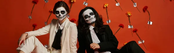 Couple dans le maquillage du crâne de sucre et costumes élégants regardant la caméra en studio avec des fleurs, bannière — Photo de stock
