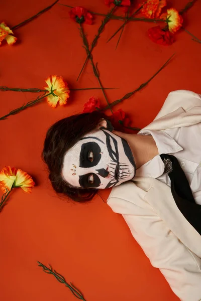 Женщина в dia de los muertos макияж и костюм лежа на красном фоне с цветами, вид сверху — стоковое фото