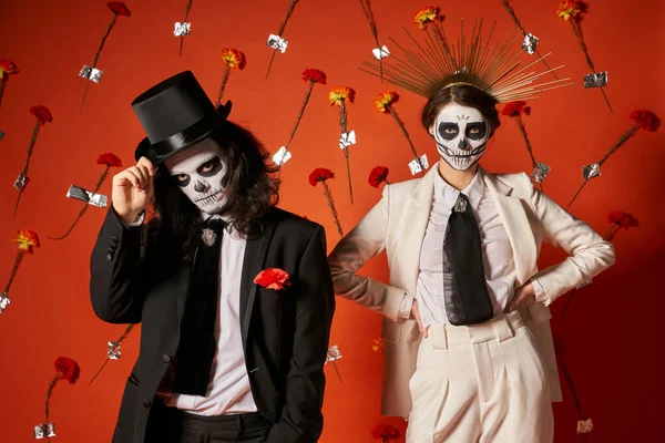 Dia de los muertos party, paar in catrina geschminkt und festlich gekleidet im roten studio mit blumen — Stockfoto
