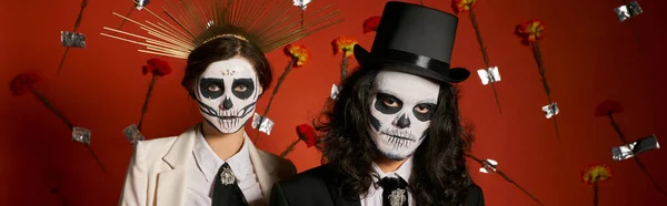 Dia de los muertos, couple in scary makeup, top hat and crown on red backdrop with flowers, banner — Stock Photo