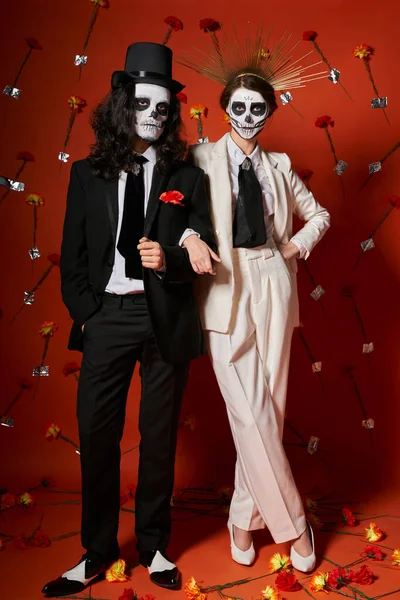 Longueur totale de couple élégant festif en dia de los muertos maquillage sur fond rouge avec décor floral — Photo de stock