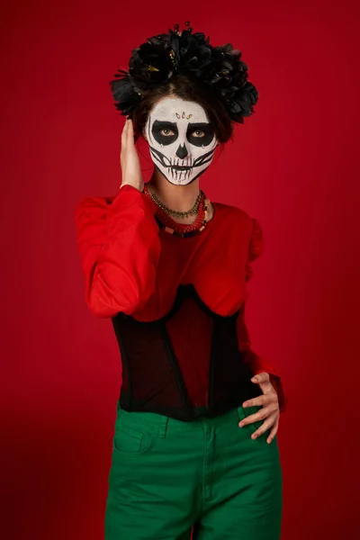 Femme dans le traditionnel dia de los muertos crâne maquillage et tenue de fête en regardant la caméra sur rouge — Photo de stock