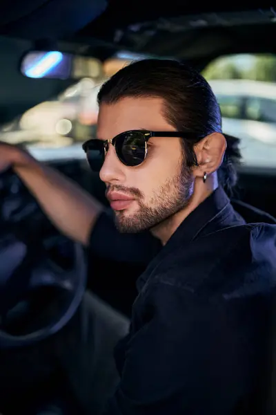 Vertical shot of handsome sexy man in sunglasses in back shirt posing in his car, sexy driver — стоковое фото