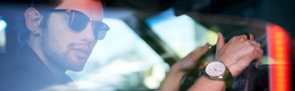 Красивый молодой человек в солнцезащитных очках позирует за рулем своей машины с наручными часами, баннером — стоковое фото