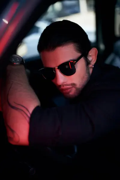 Sexy junge Fahrerin mit Tätowierung und Sonnenbrille posiert am Steuer des Autos und blickt in die Kamera — Stockfoto