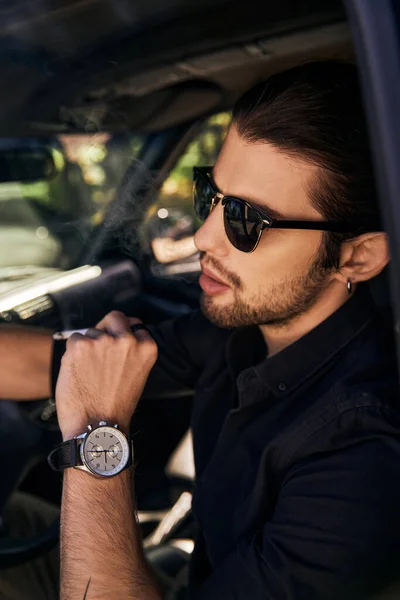 Good looking young man with sunglasses and wristwatch sitting in his car and posing in profile — Stock Photo