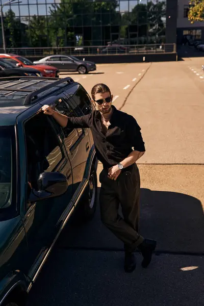 Вертикальний знімок привабливого чоловіка в чорному одязі з аксесуарами, що позують біля його машини, концепція моди — стокове фото