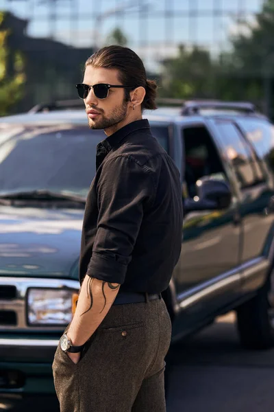 Tempting stylish driver in elegant black attire with tattoo and earring with hands in pockets — Stock Photo