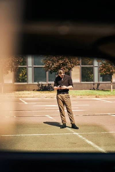Вертикальный снимок заманчивого человека в черном, смотрящего на свой телефон, прежде чем позвонить своему страховщику — стоковое фото