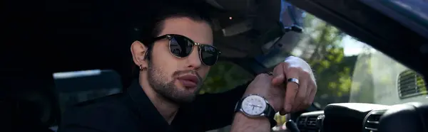 Young elegant man with wristwatch and sunglasses behind steering wheel and looking at camera, banner — Stock Photo